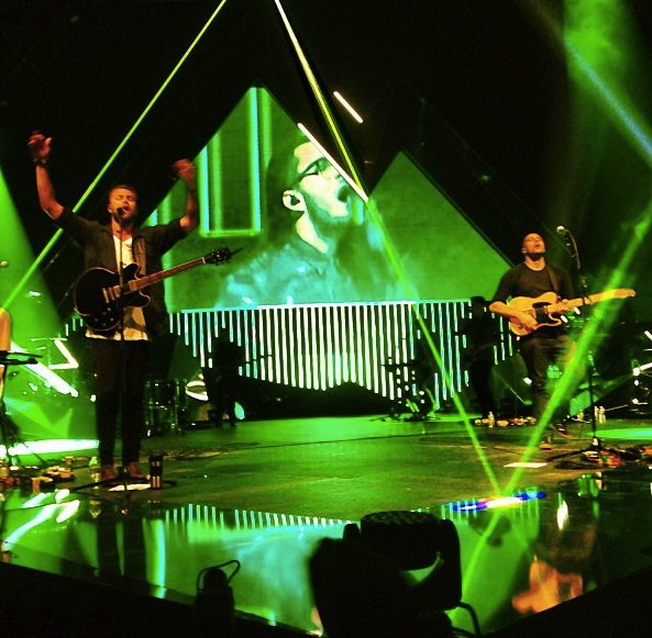 Hillsong United onstage under green laser beams