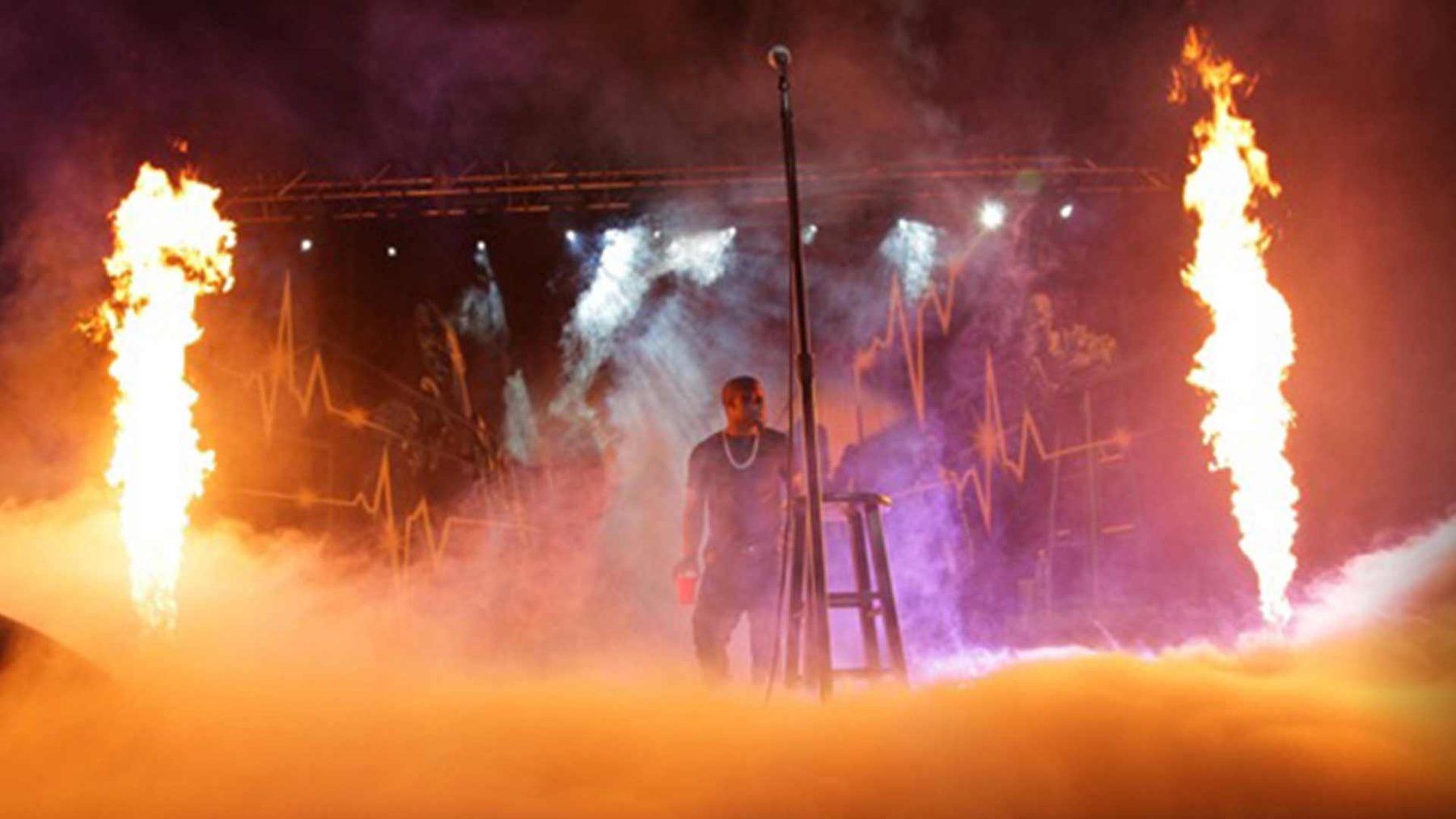 Kevin Hart onstage between flame columns and low fog