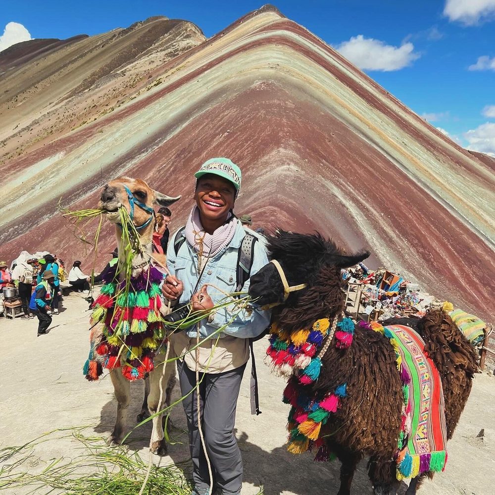 Genell smiling between two llamas in tasseled harnesses at Rainbow Mountain, Peru